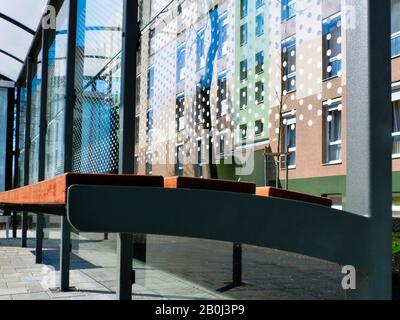 modern bus shelter detail with aluminum frame & polka dotted glass structure with residential building in background in strong diminishing perspective Stock Photo