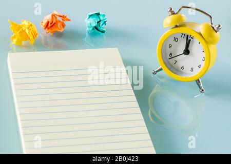 A yellow alarm clock next to swept balls of paper and a notebook. Place for text. Office concept Stock Photo