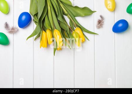 Decorative eggs and yellow tulips on white background Stock Photo
