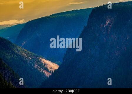 Sunrise over deep blue green canyon, orange and yellow clouds in the sky, bright spot of sunlight on canyon walls. Stock Photo