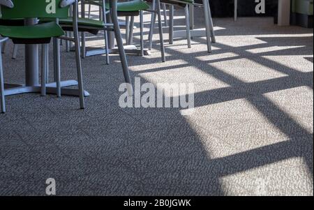 Sunbeam from a window in an airy cafe creates a pattern on this grey carpeted floor Stock Photo