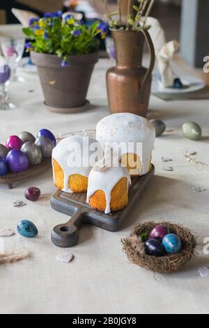 Naturally dyed Easter quail eggs in nest, Easter cakes, fresh violets potted, wooden hearts background, retro styled spring holiday greeting postcard Stock Photo
