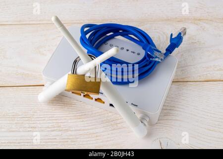 Padlock on Wi-Fi wireless router antennas and disconnected network cable on a wooden table. Forbidden or limited internet and internet censorship. Stock Photo