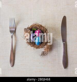 Easter festive spring table setting decoration, naturally dyed quail eggs in nests, feathers, wooden hearts, family dinner or breakfast concept Stock Photo
