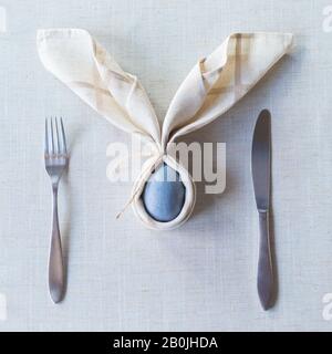 Easter festive spring table setting decoration, bunny ears shaped napkins, dyed eggs, family dinner or breakfast concept Stock Photo