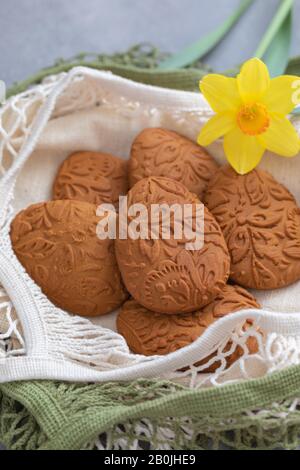 Easter egg shaped ginger cookies on the kitchen towel background, with fresh daffodil flower Stock Photo