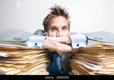 Overwhelmed office worker resting on the huge pile of paperwork on his desk Stock Photo