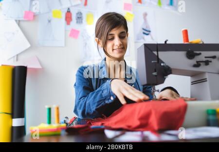 Young fashion designer sewing at workshop. Tailor working on sewing machine. Small business concept. Stock Photo
