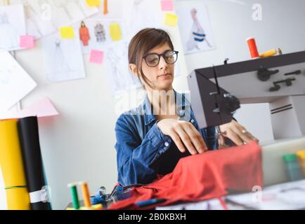 Young fashion designer sewing at workshop. Tailor working on sewing machine. Small business concept. Stock Photo