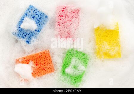 Multicolored soapy sponges with foam on white background. Cleaning concept, top view Stock Photo