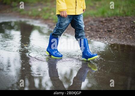 Little boy in raincoat and rubber boots playing in puddle Stock Photo