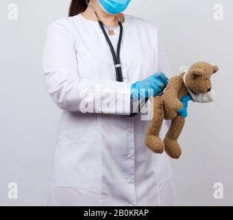 female medic holds brown teddy bear with paw bandaged in white bandage and listens to toy with stethoscope, concept of pediatrics and animal treatment Stock Photo