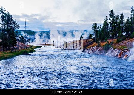 Blue river flowing from geysers and hills with green pine trees on both sides of river banks. Stock Photo