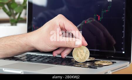 man checking cryptocurrency chart and bitcoin coins on a laptop Stock Photo