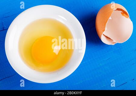 Bright yellow egg yolks in a white bowl on wooden background. Stock Photo