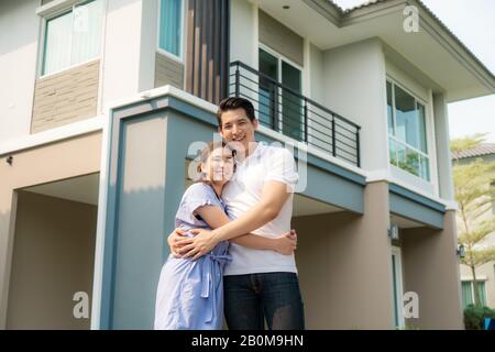 Portrait of Asian young couple standing and hugging together looking happy in front of their new house to start new life. Family, age, home, real esta Stock Photo