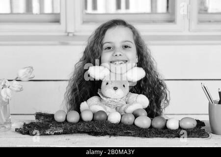 rabbit or hare toy, easter colorful eggs, pencils, tulip flower, cute girl, happy small child with curly hair near window, womens or mothers day spring holiday Stock Photo