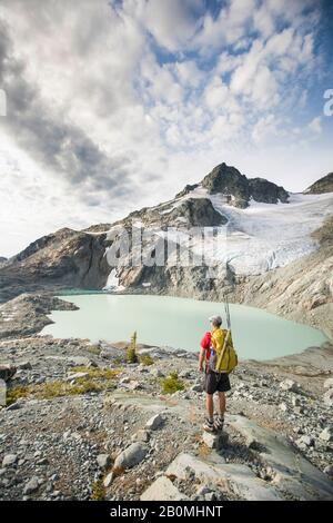 Backpacker stops to look at view of mountains glacier and lake. Stock Photo