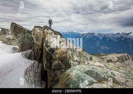 Rear view of climber standing on rocky summit ridge.