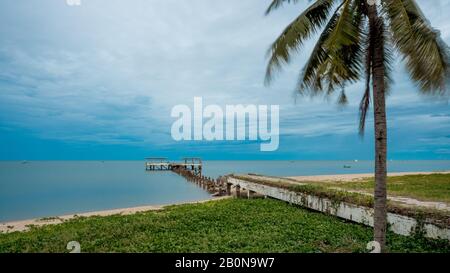 palm tree and walkway leading to Dilapidated old fishing dock collapsing into the sea in Pak Nam Pran on the Gulf of Thailand in Thailand Stock Photo