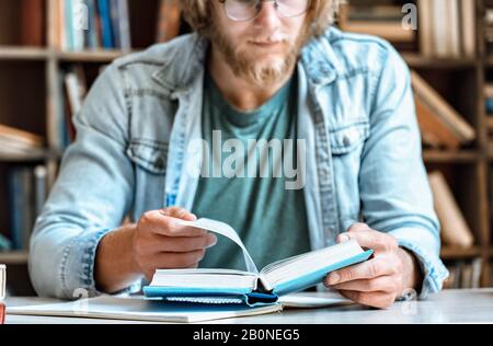 Closeup young man home library desk open read book turn page education concept Stock Photo
