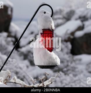 A beautiful red hummingbird feeder is covered with snow with the sunlight shining through it. Stock Photo