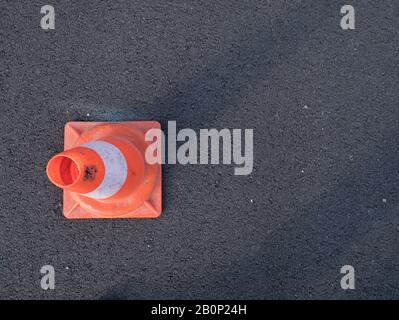 Traffic cone with shadow on asphalt. Traffic cone, with white and orange stripes on gray asphalt, copy space. Stock Photo