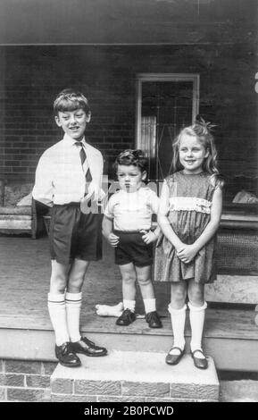A 1969 black and white image of three Australian white children, well dressed and standing at the top of a small set of stairs to a home in Sydney. Stock Photo