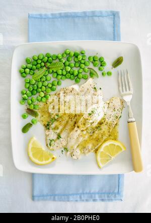 Wild pacific poached sole fillets drizzled with lemon butter sauce and organic minty peas.  White plate in flat lay composition and shot in natural li Stock Photo