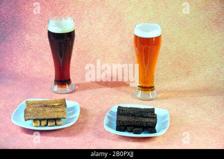 Two tall glass glasses with light and dark beer and two plates with wheat and rye croutons on a brown background. Close-up. Stock Photo