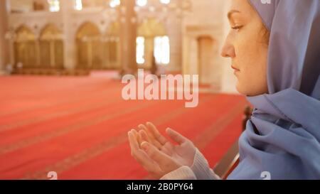 thoughtful woman in blue headscarf prays holding hand palms up standing in ancient mosque extreme copyspace Stock Photo