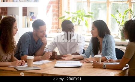 Horizontal photo diverse employees team discussing project at meeting, colleagues listening to Asian businesswoman, colleagues sitting at office table Stock Photo