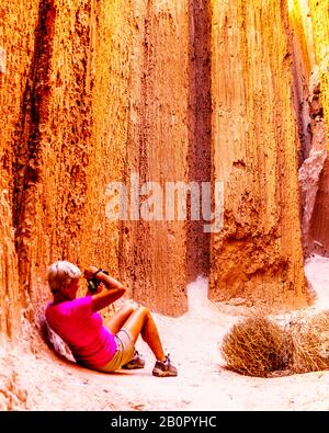 A senior woman taking a photo of he dramatic and unique patterns of Slot Canyons in Cathedral Grove State Park in the Nevada Desert, United States Stock Photo