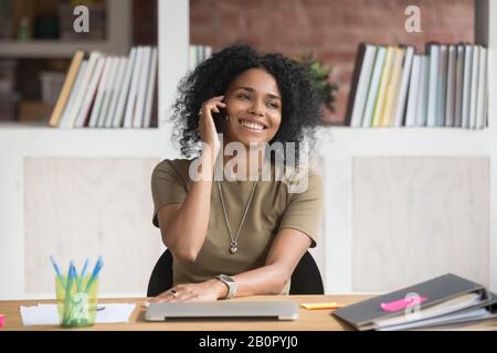 Smiling African American businesswoman talking on phone at work, friendly female manager, advisor consulting client, having pleasant conversation, emp Stock Photo