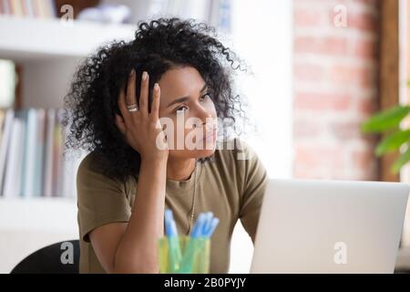 Bored African American businesswoman disinterested in routine monotonous work, unmotivated female employee or student holding head on hand, rolling ey Stock Photo