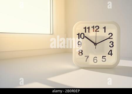 Rectangular white alarm clock on sunny window background. Stock Photo