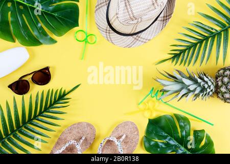 Colorful summer composition with straw hat, sunglasses, palm branche, pineapple and flip flops on yellow background top view. Summer fashion, vacation Stock Photo