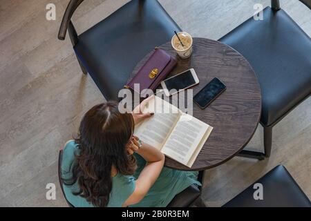 Overhead view of Asian lady reading book at coffee table Stock Photo