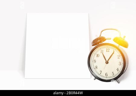 time management concept. analog vintage black clock with blank white paper leaning against the white wall. blank white paper with copy space for your Stock Photo