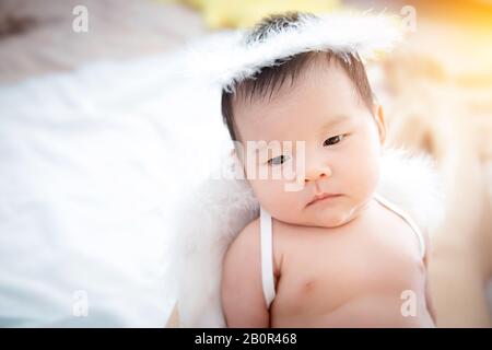 Close-up beautiful newborn baby girl. A portrait of a beautiful newborn baby girl wearing angel wings and angel ring. Stock Photo