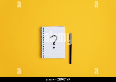 Question mark drawn on notepad with black marker lying next to it. Over yellow background with copy space. Stock Photo