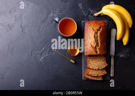 Banana, coconut bread, cake with cup of tea on slate board. Dark stone background. Copy space. Top view. Stock Photo