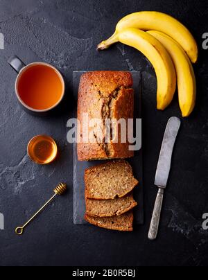 Banana, coconut bread, cake with cup of tea on slate board. Dark stone background. Top view. Stock Photo