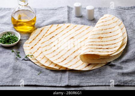 Tortillas, flat breads with olive oil on grey textile background. Stock Photo