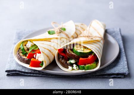 Wrap sandwich with grilled vegetables and feta cheese on a plate. Grey background. Close up. Stock Photo