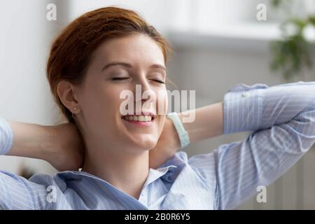 Close up smiling businesswoman relaxing in comfortable chair after finished work at workplace, daydreaming about good future, visualization, satisfied Stock Photo