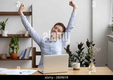 Satisfied businesswoman stretching at workplace after finished work, sitting in comfortable chair, happy employee with closed eyes relaxing during bre Stock Photo