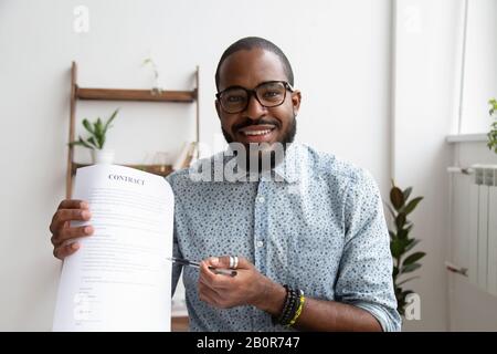 Head shot portrait smiling African American businessman proposing to sign contract to client, looking at camera, sitting at desk, employee holding pap Stock Photo