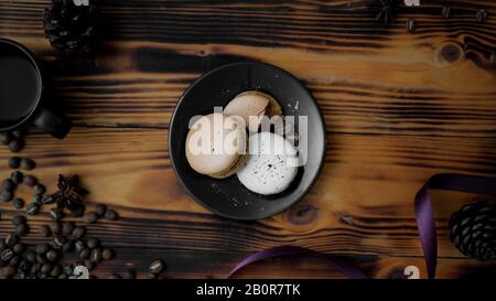 Top view of Coffee macarons on black plate with purple ribbon, coffee bean and dry roses decorated on rustic table background Stock Photo