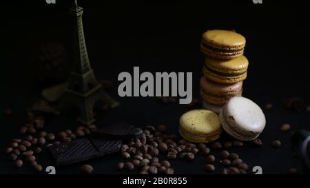 Cropped shot of coffee and chocolate macarons on coffee bean with Eiffel Tower model decorated on dark background Stock Photo